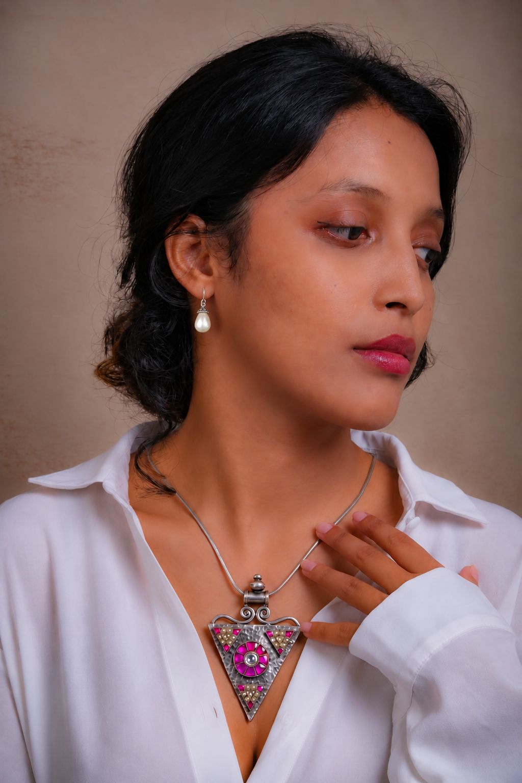 A Totapari model in a white open-collar shirt wearing pearl drop earrings and a silver pendant sitting inside the collar opening.